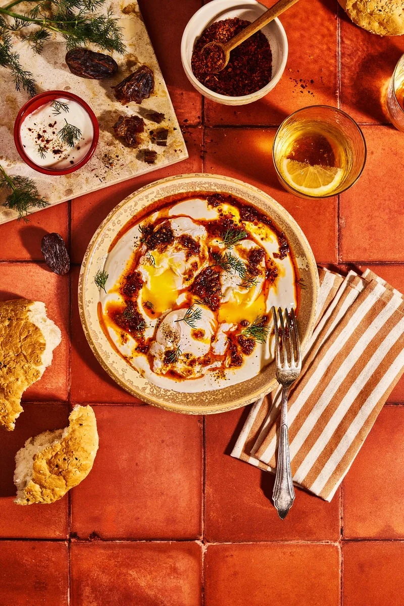 Türkische Eier mit scharfer Dattelbutter, Brot und Gewürzen auf terrakottafarbenen Fliesen